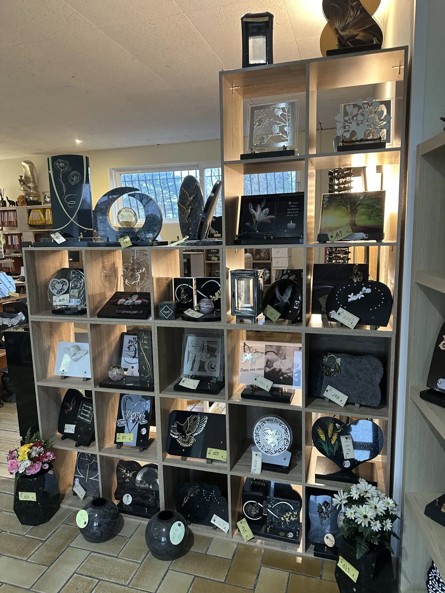 Meuble étagère d'exposition présentant diverses plaques funéraires, lanterne et urnes en magasin