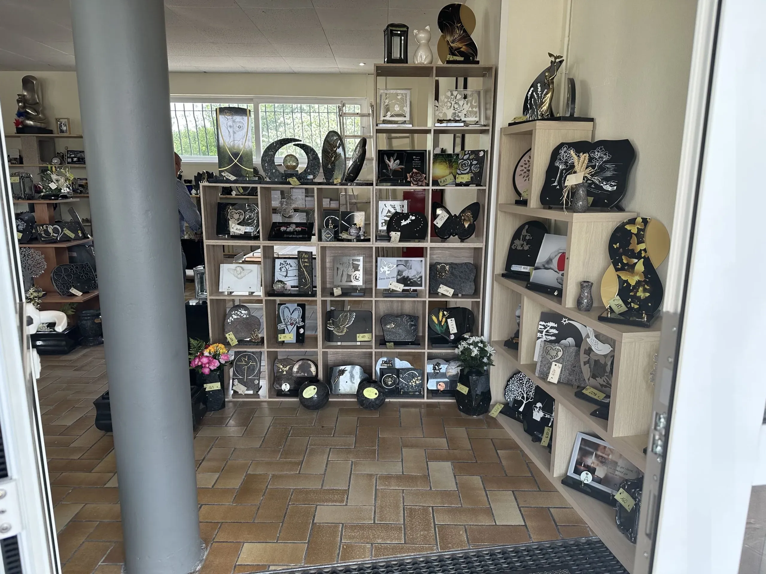Entrée du magasin de marbrerie avec rayonnages et étagères présentant des plaques funéraires