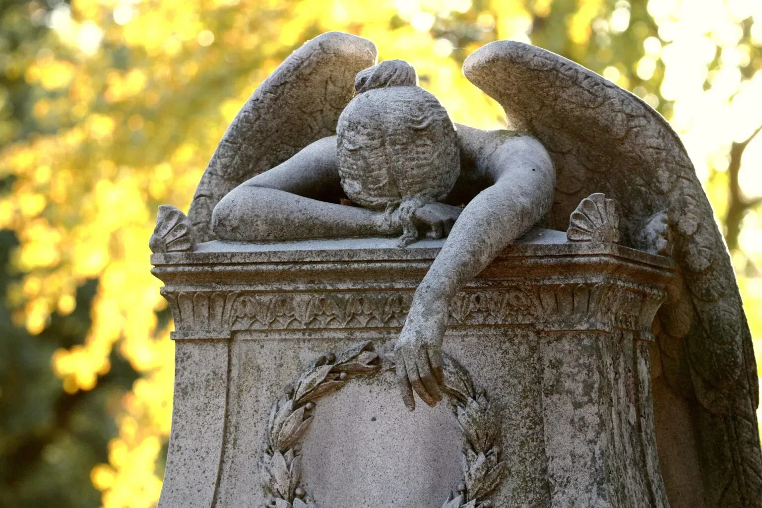 Statue d'ange pleureur sculptée en pierre penchée sur une stèle funéraire
